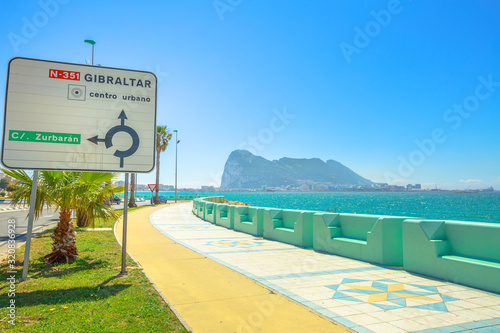 The Rock of Gibraltar, British territory, and its bay view from Spanish territory of La Linea town. directions road sign of Gibraltar center on the waterfront promenade.