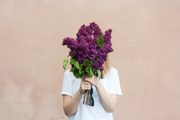 Woman holding a vivid bunch of lilac flowers against brick wall