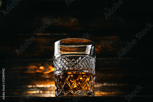 glass of whiskey with ice on a wooden table surrounded by smoke