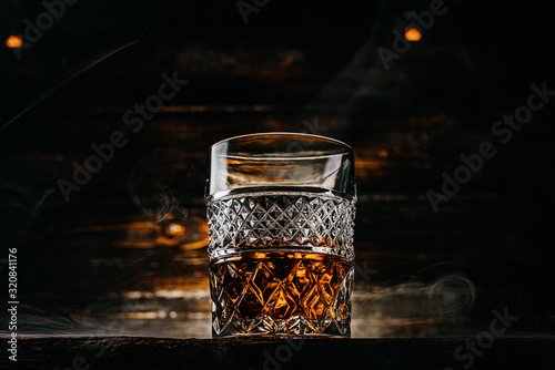 glass of whiskey with ice on a wooden table surrounded by smoke