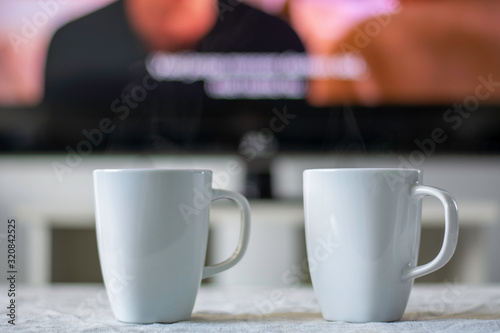 Coffee mugs with a television screen with a movie and subtitles in background. photo