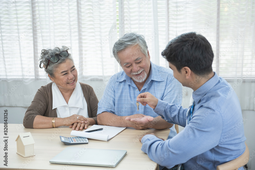 Smiling satisfied senior couple making sale purchase deal concluding contract hand get house key from real estate agent,happy older family and broker shake hands agreeing to buy new house at meeting.