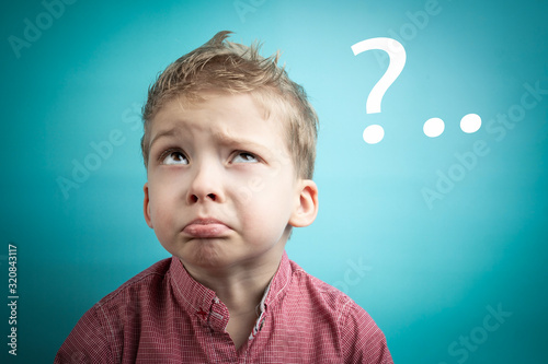 child asks a lot of questions. child thinks and looks up. first grader strains the brain. the boy in the red shirt on a blue background
