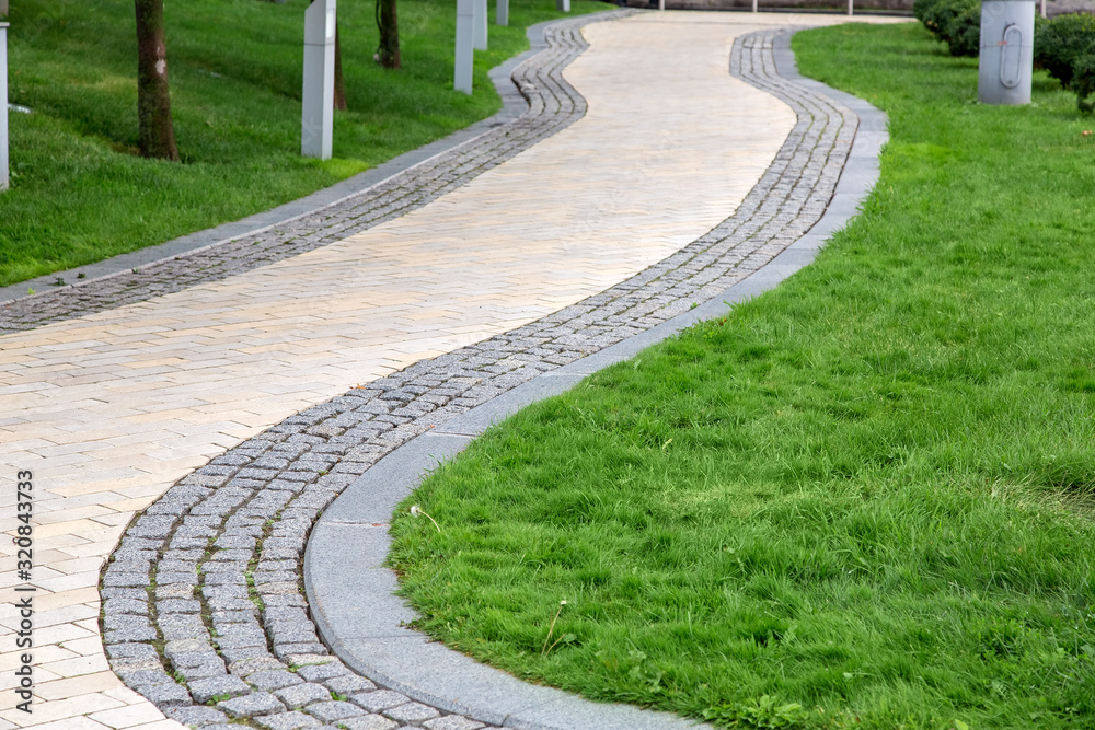 winding pedestrian walkway made of stone tiles in a park with a green lawn, nobody. winding pedestrian walkway made of stone tiles in a park with a green lawn, nobody.