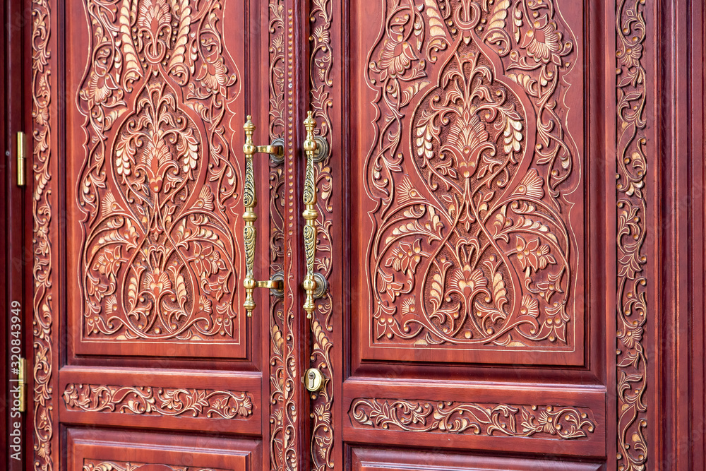 brown front door with a pattern of wood carvings with iron handles and keyhole, close up details. brown front door with a pattern of wood carvings with iron handles and keyhole, close up details.
