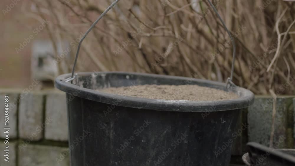 Builders black plastic bucket full of sand tilting shot Builders black plastic bucket full of sand tilting shot