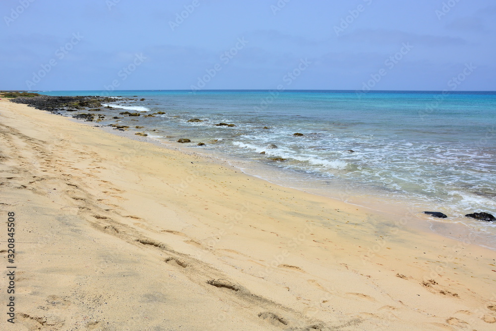 A sandy beach and blue, turquoise ocean, sea with rock on the shore