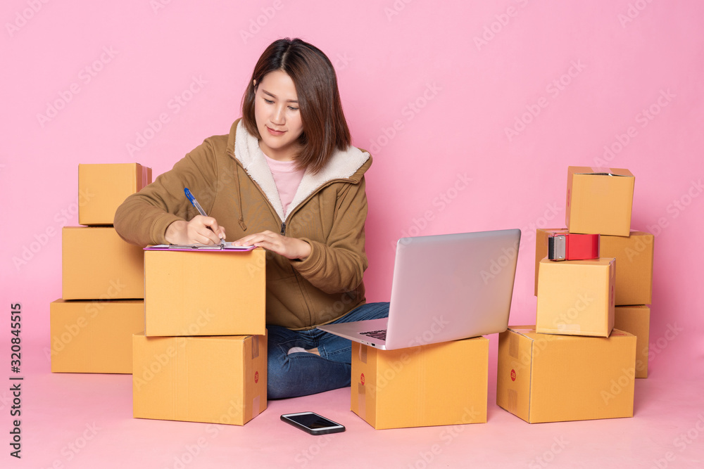 An Asian woman in a yellow coat Checking orders from customers on laptops and mobile phones.On the pink background, online businesses and delivery concepts