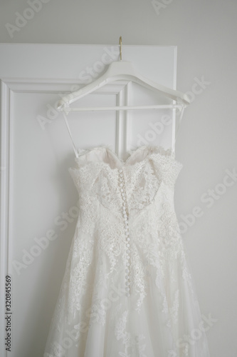 White dress of the bride hangs on a wooden door. Wedding accessories.