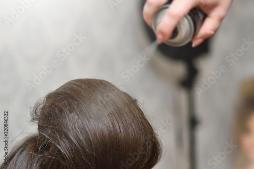 Female head and hair spray. The girl the hairdresser applies hair spray when creating a voluminous hairstyle in a beauty salon.