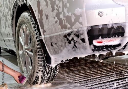 The hand of the working cleanser brushed the bottom of the wheel and drive the car in soap foam.