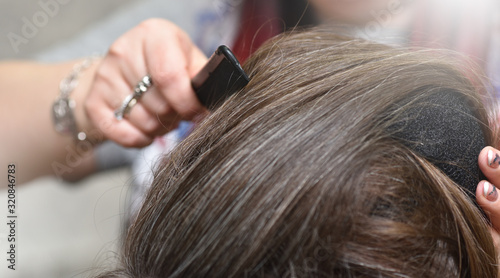 Hairdresser combs female hair with a black plastic comb while creating a hairstyle in a beauty salon