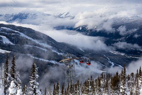 Whistler, British Columbia, Canada. Beautiful View of Peak to Peak Gondola with the Canadian Snow Covered Mountain Landscape during a cloudy and vibrant winter sunset photo