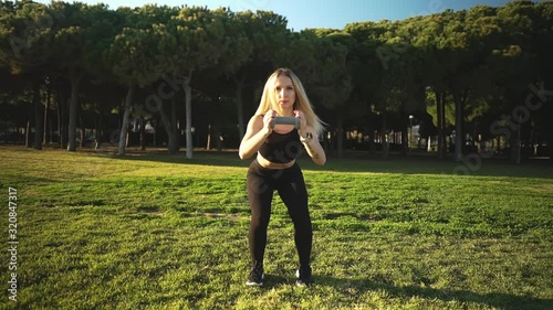 Sport training in city park. Beautiful caucasian fit woman gets in shape with dumbbells. Freeweight leg training outdoors photo