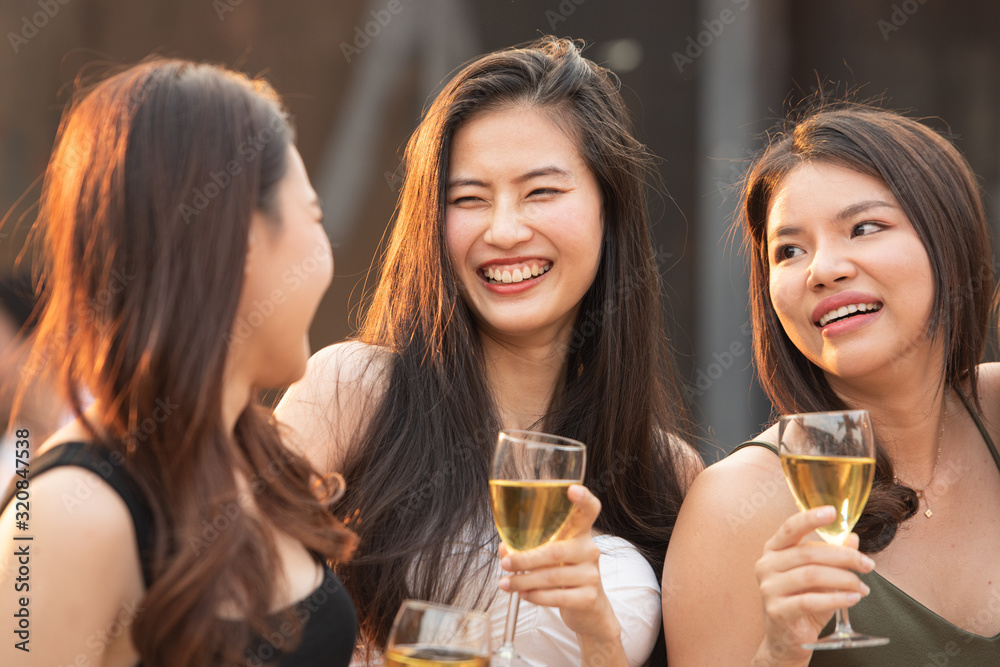 Group of young beautiful happy asian women holding glass of wine chat together with friends while celebrating dance party on outdoor rooftop nightclub,leisure lifestyle of young friendship concept.