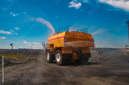 Heavy truck pours the road with water in the iron ore quarry. Dust removal, protection of the environment. Irrigation of the road from dust