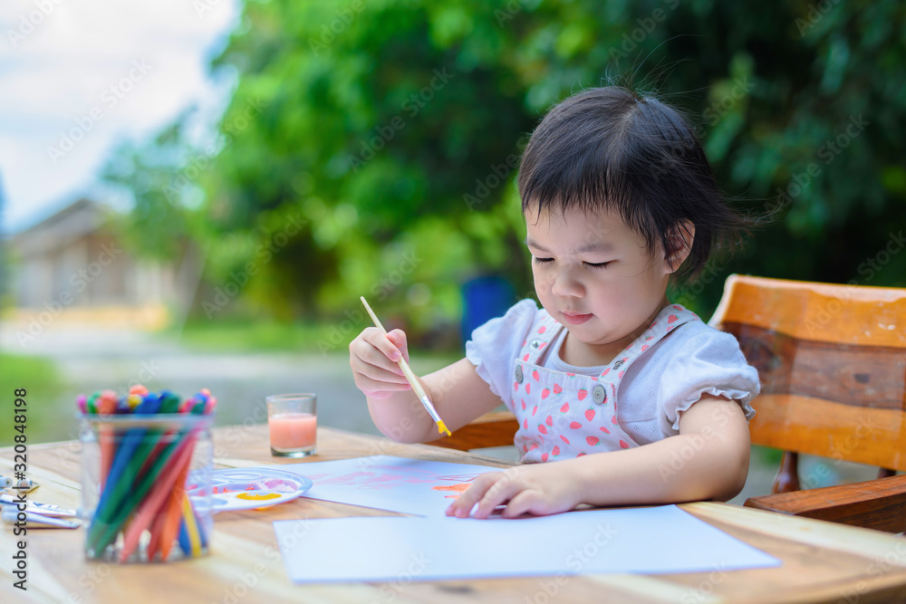 Cute little Asian girl in a white dress is drawing with painting fun Cute little Asian girl in a white dress is drawing with painting fun
