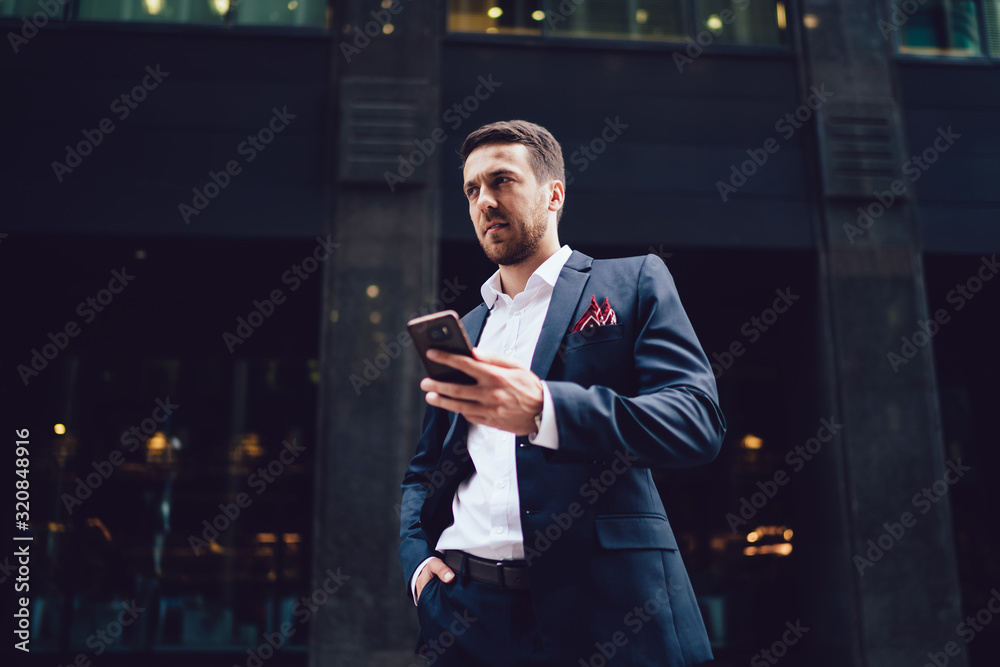 Fototapeta premium Bewildered businessman with smartphone in city