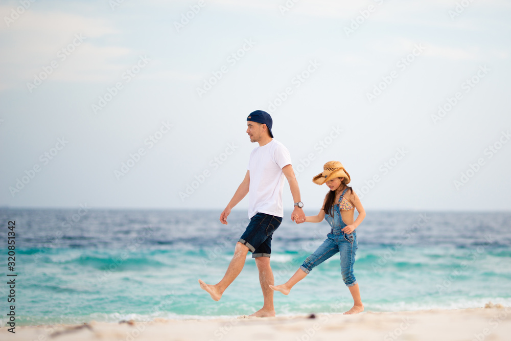 ビーチで手をつないで歩く父と娘