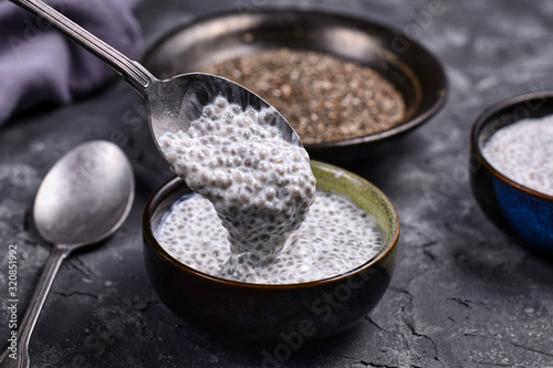 Spoon filled with chia seed pudding made with dry seeds soaked in milk in small bowls with dry seeds in background photo