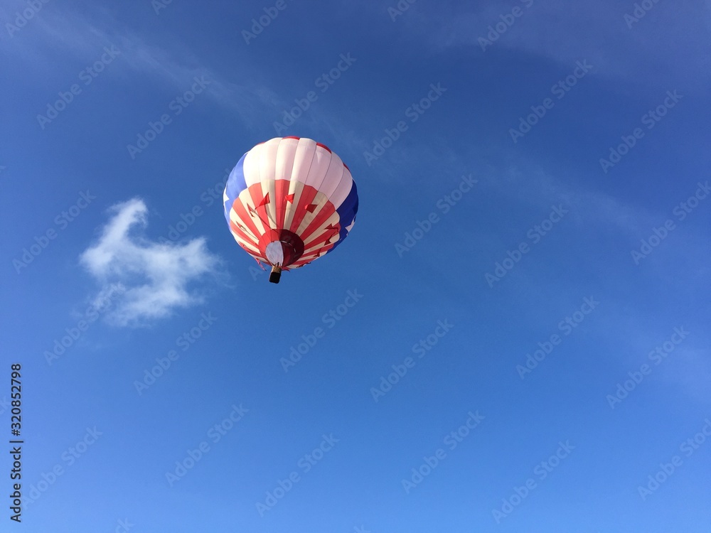 Single red, white and blue hot air balloon floating up into a blue sky, further Single red, white and blue hot air balloon floating up into a blue sky, further