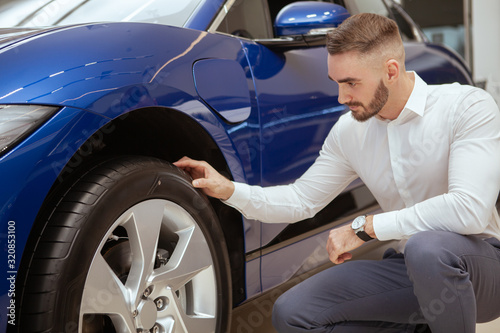 Handsome bearded man examining tires on a new car on sale at the dealership