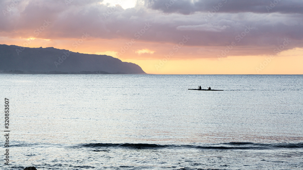 Obraz premium Outrigger canoes at sunset at Haleiwa Hawaii Oahu orange clouds with blank space for copy