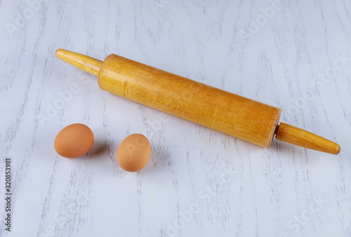 Rolling pin and two eggs on white table.