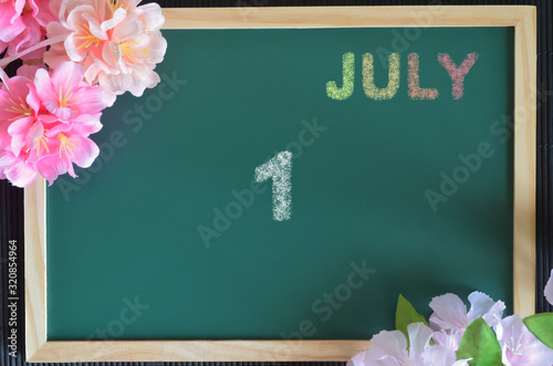 Date 1, July month write with colorful chalk, flowers on the board.