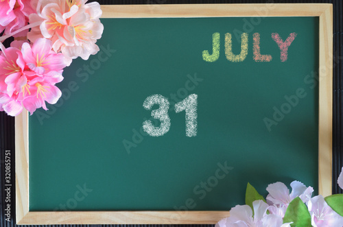 Date 31, July month write with colorful chalk, flowers on the board.