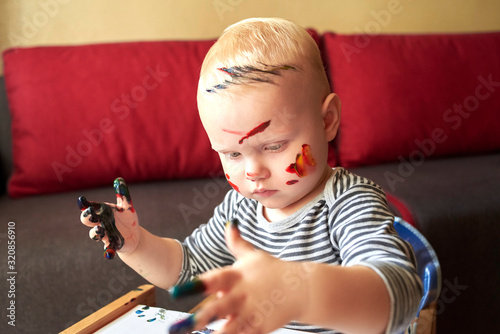 An smeared little boy draws with finger paints.