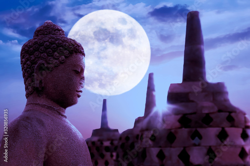 A statue of Buddha against the background of the moonlight in the temple of Borobudur.  Java island. Indonesia. Famous historical place. Outside. photo