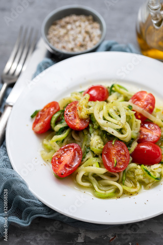 Spiral zucchini noodles with tomato on white plate on ceramic background