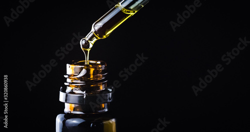 CBD Hemp oil, Hand holding droplet of Cannabis oil against black background. Alternative Medicine photo