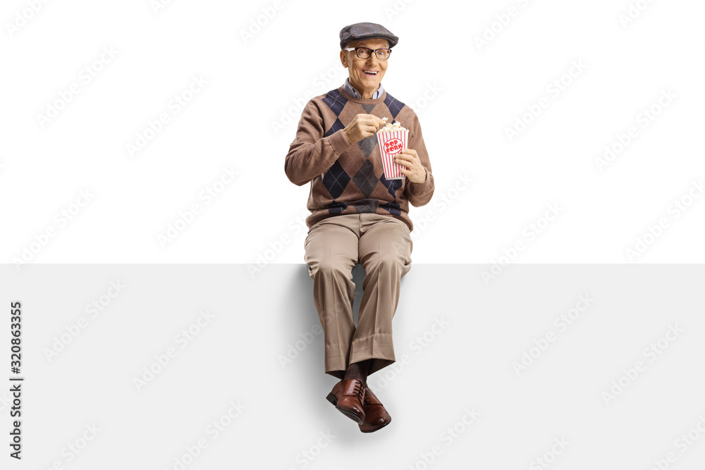 Senior man sitting on a panel eating popcorn and miling at camera