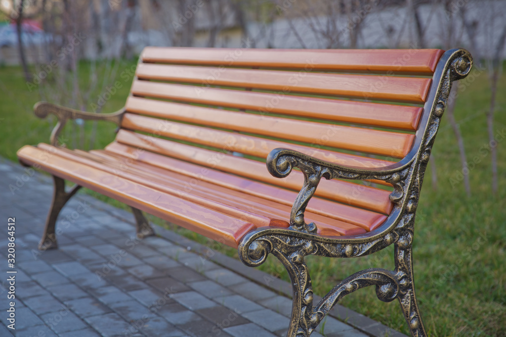 Wood exterior material. Wood material details. Blank Old bench in a shady area of the garden or the park,outdoor. Shaded wood park bench surrounded by greenery . Empty Park wooden bench Closeup view.