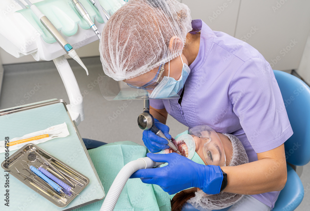 The dentist using specialized tools treats caries in the patient’s oral