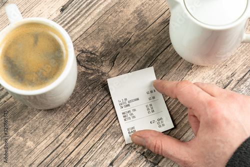 a hand on a receipt on a table with a cup of coffee