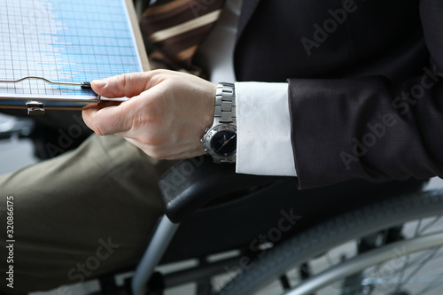 Disabled man holds business chart in hand while sitting wheelchair closeup office background. Adaptation of people with disabilities in society concept