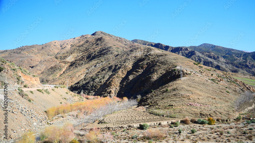 Fototapeta premium Bright landscape of Morocco, breathtaking curves of mountains, stunning combination of hills & farm land,inadvertent distribution of houses & huts, raw impression of pure nature.