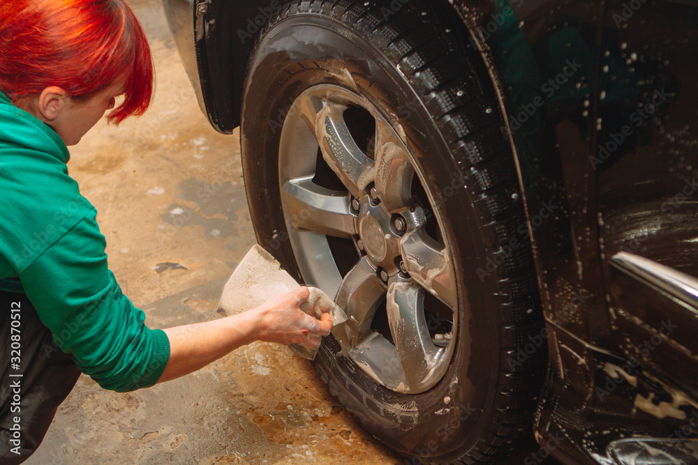 An employee of the car wash thoroughly washes conducts detaling and applies protective equipment to the body of an expensive car.