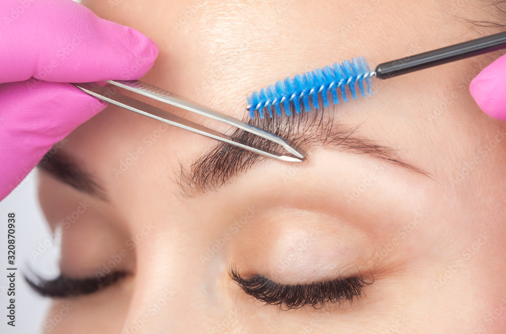 Make-up artist plucks eyebrows with tweezers to a woman before staining with henna.Makeup concept, eyebrow shape modeling and eyelash extensions.