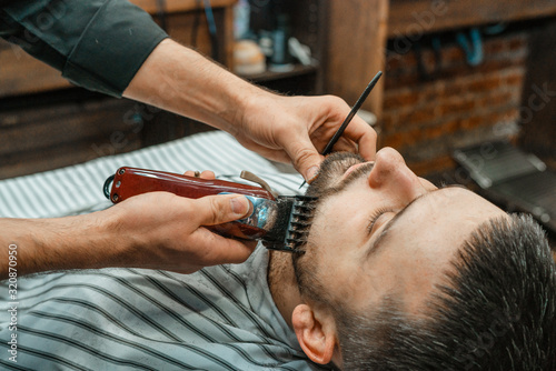 Beauty shop for men. Shaving a beard in a barbershop. Barber cuts his beard with a razor and clipper. close up Brutal haircuts. Hairdresser equipment. Selective focus.