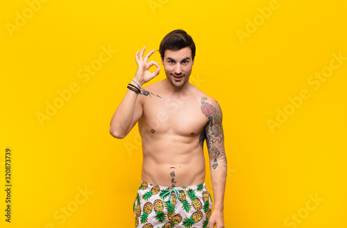 young handsome man feeling successful and satisfied, smiling with mouth wide open, making okay sign with hand photo