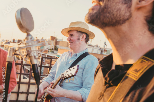 Small rock pop band playing on a rooftop with sunset on the background. Man in adult age performing on summer season. Music live concerts concept. photo