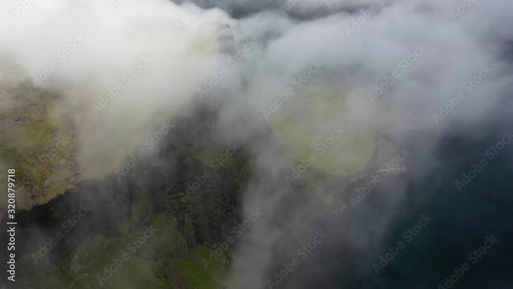 Rugged Faroe Islands coastline through sea clouds, high aerial birds eye view