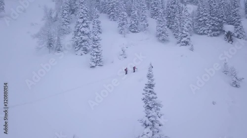 DRONE SHOT Skiers walking up the mountain while snowy weather, touring in the alps photo