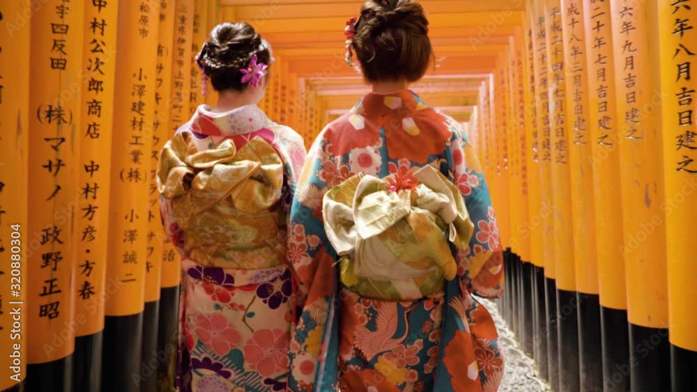 Geisha wearing kimono with flowers in hair walking through the Fushimi Inari-Taisha shrine in Japan
