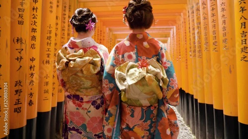 Geisha wearing kimono with flowers in hair walking through the Fushimi Inari-Taisha shrine in Japan photo