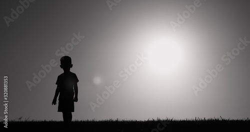 Silhouette of little boy standing in a grass field. 